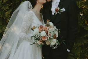 Close-up of wedding couple with bride holding peach and white floral bouquet.