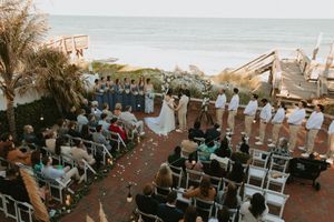 Oceanfront wedding ceremony setup with rows of white chairs and floral decorations at sunset.