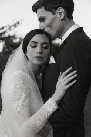 Intimate black and white portrait of newlyweds sharing a tender moment with bride in lace dress and veil.