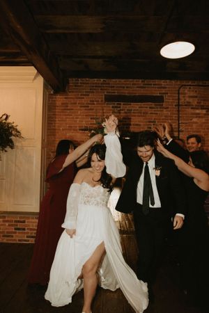 Wedding party celebrates on dance floor with raised hands and joyful energy.