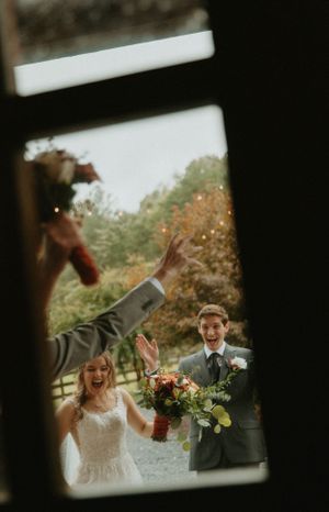 Candid wedding photo through a window frame showing couple reacting to confetti toss.