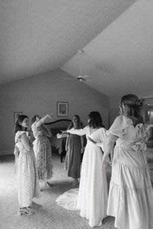 Black and white photo of bridesmaids in flowing dresses celebrating in a bedroom.