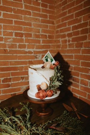 White wedding cake with floral decorations displayed against exposed brick wall.