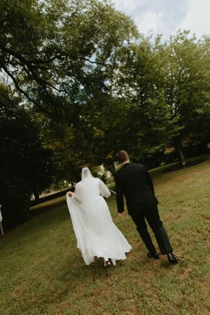 A couple walks up a grassy hill together in wedding attire.