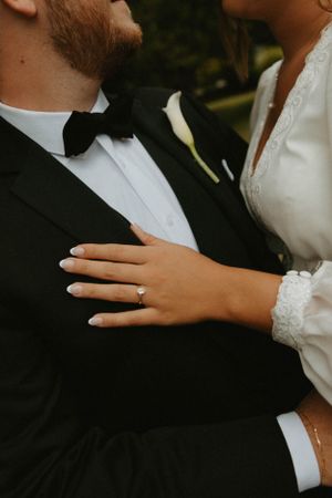 Close-up of a wedding ring and lace sleeve details against a formal tuxedo.