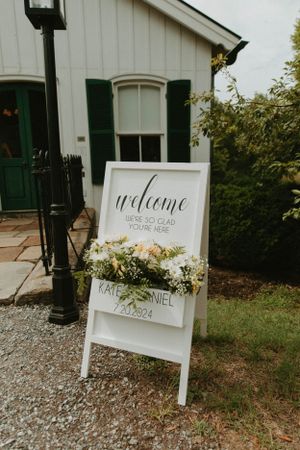 White welcome sign with floral decorations outside a classic white building.