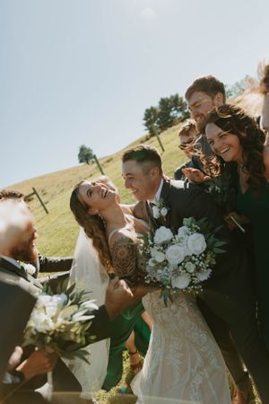 Candid wedding photo of bridal party laughing together outdoors with white bouquet.