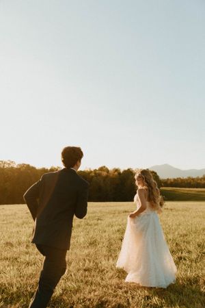 Wedding photographer captures bride and groom in golden sunset light across meadow.