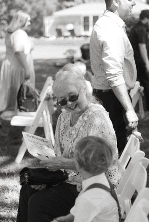 Guest in lace dress reading program during outdoor wedding ceremony.