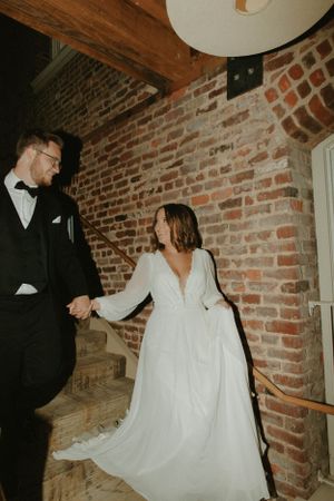 A wedding couple descends rustic brick stairs in elegant attire.