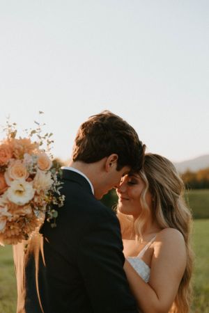 Intimate moment between newlyweds with peach floral arrangement at sunset.