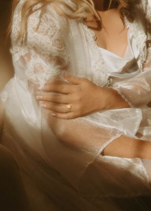 Close-up detail of delicate lace wedding dress fabric and hands.