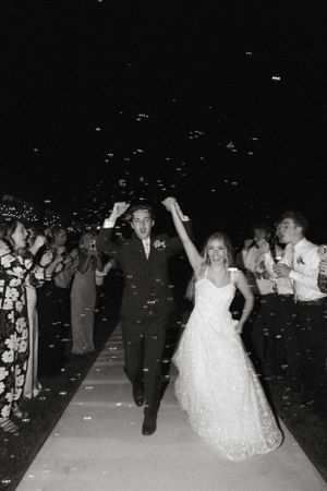 Newlyweds exit their celebration under floating bubbles at night.