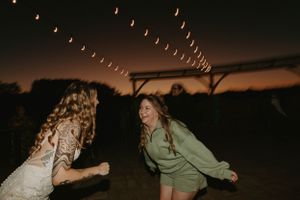 Two women dancing under string lights at outdoor evening reception.