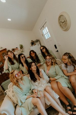 Group of bridesmaids in mint green dresses laughing together on indoor couch.