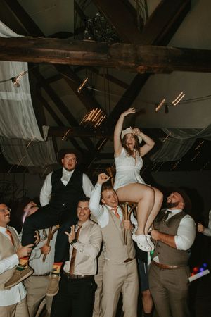 Wedding party celebrates with energetic dance moves under rustic wooden beams.