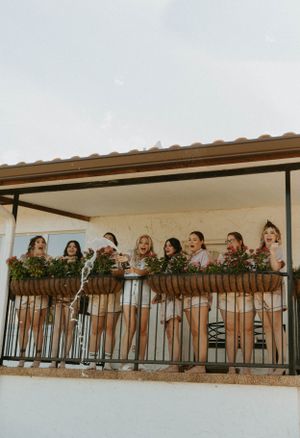 Bridesmaids in matching dresses lean against a balcony railing while holding bouquets.