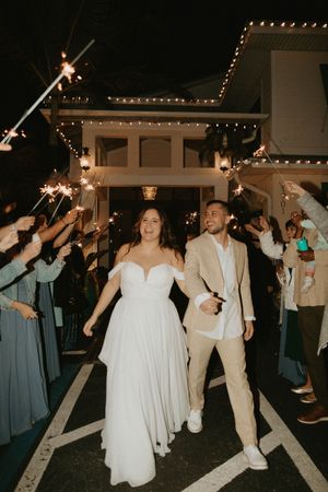Newlyweds exit their reception under sparklers held by guests at night.