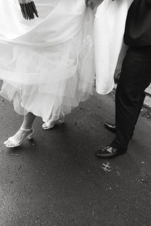 Black and white detail shot of wedding dress hem and formal shoes.