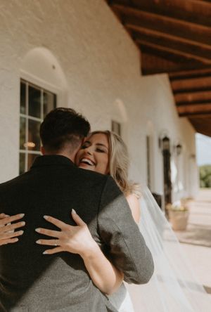 A joyful embrace captured during a wedding moment on a white-walled porch.