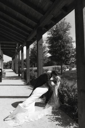 A dramatic black and white wedding photo of a couple kissing under a covered walkway.