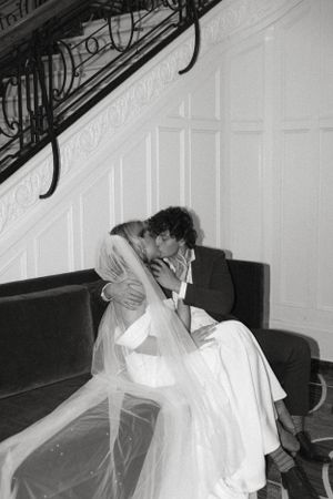 Romantic black and white photo of newlyweds embracing on a vintage couch under a staircase.
