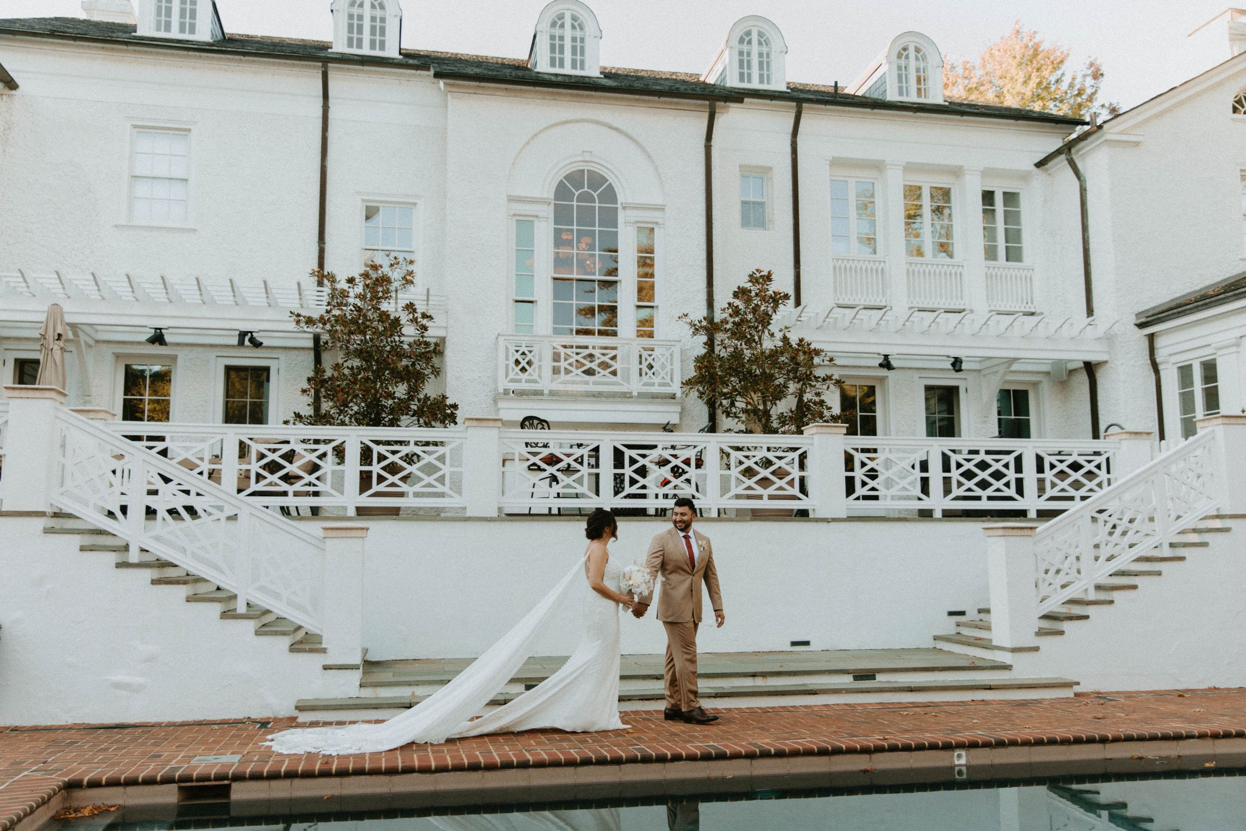 Newlyweds pose on grand white stairs of an elegant building with architectural details.