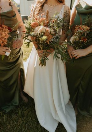 Beautiful autumn-colored wedding bouquets held against green and white dresses.