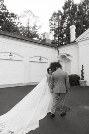 A couple walks along a white building exterior with elegant arches and a flowing wedding veil.