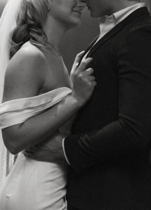 Intimate black and white portrait of newlyweds in formal attire sharing a close moment.