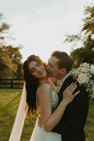 Romantic sunset portrait of newlyweds embracing in a field with white floral bouquet.