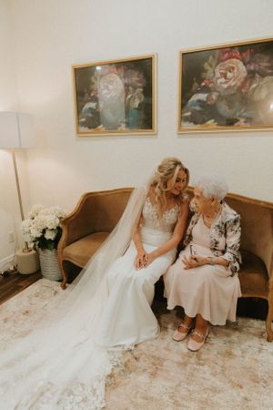 A tender moment shared between a bride and an elderly woman on a vintage brown couch.