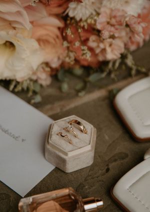 A delicate hexagonal velvet ring box sits among pink flowers and wedding details.