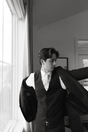 Black and white photo of a well-dressed person in formal attire looking out a window.