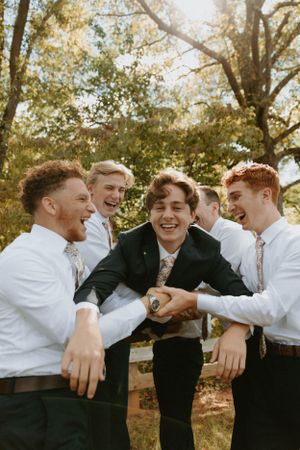 A joyful group of groomsmen sharing laughs outdoors on a sunny day.