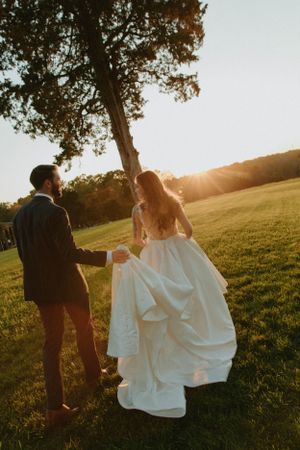 A couple dances together in a sunlit field during their wedding photoshoot.