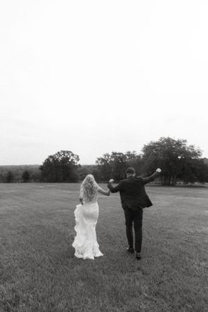 Black and white photo of newlyweds celebrating while walking across an open field.