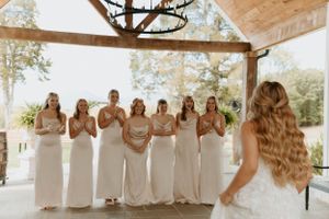 Bridesmaids in white dresses react emotionally during a first look moment under a covered venue.
