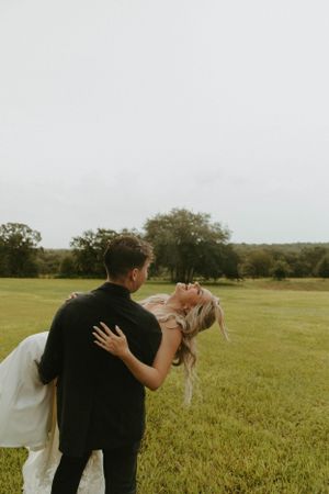 Candid moment of newlyweds dancing and laughing together in a sun-lit field.