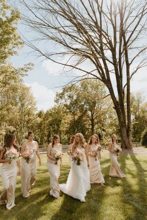 Bridal party walking through a sun-drenched garden carrying floral bouquets.