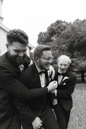 Black and white candid moment of groomsmen laughing together outside.