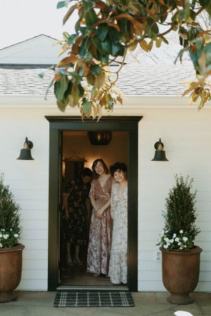 Classic white farmhouse entrance with potted plants flanking the dark wood door and decorative lantern lights.