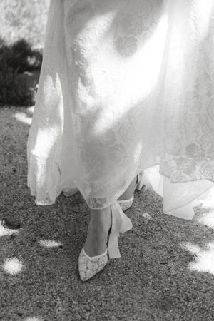 Close-up black and white photo of lace wedding shoes worn with a flowing white dress.