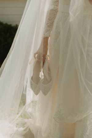 Delicate lace wedding shoes held against flowing white tulle and lace fabric.