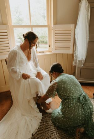 Getting ready moment in a sunlit room with wedding dress preparations.