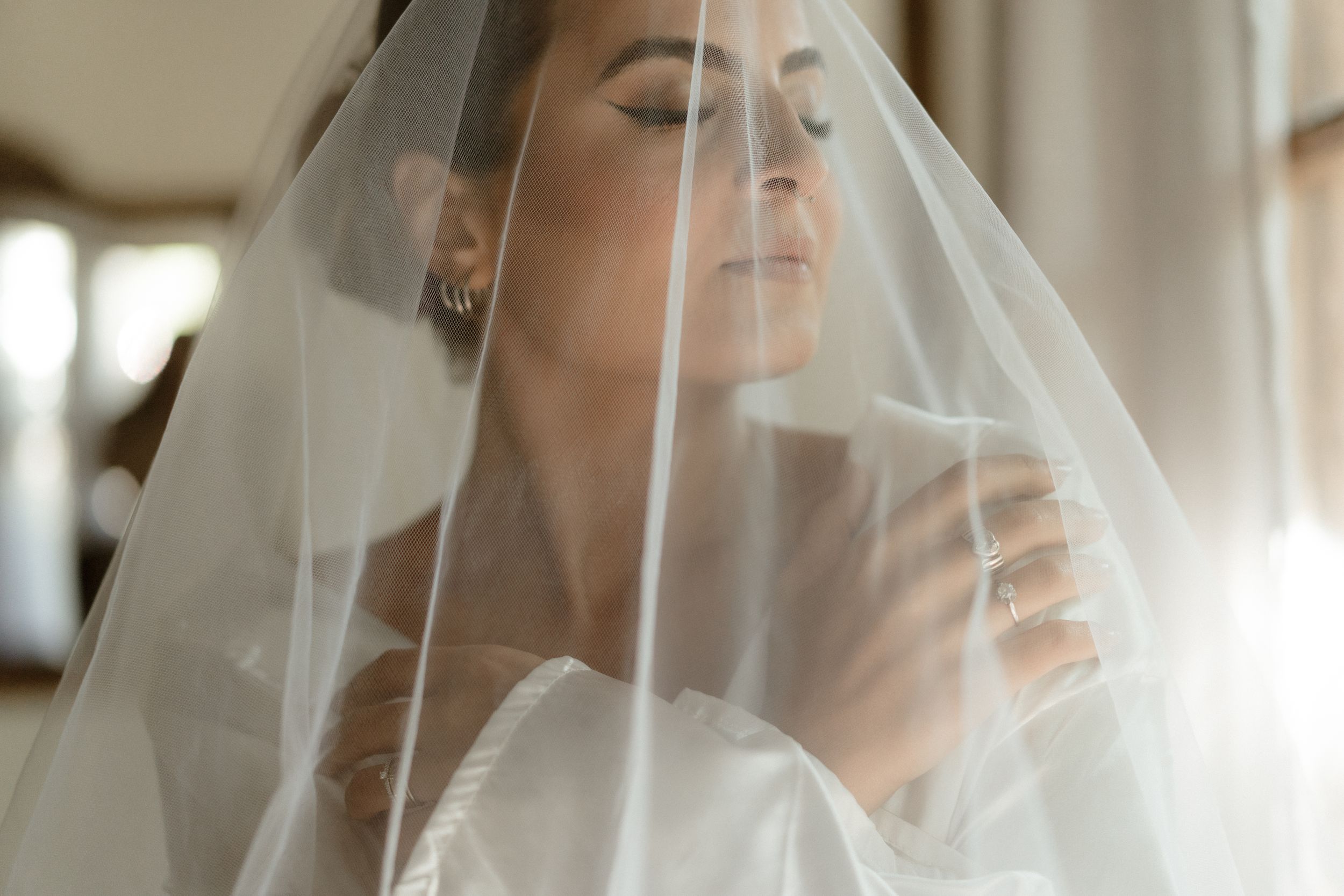 Bridal portrait in soft light with flowing veil against rustic wooden backdrop.