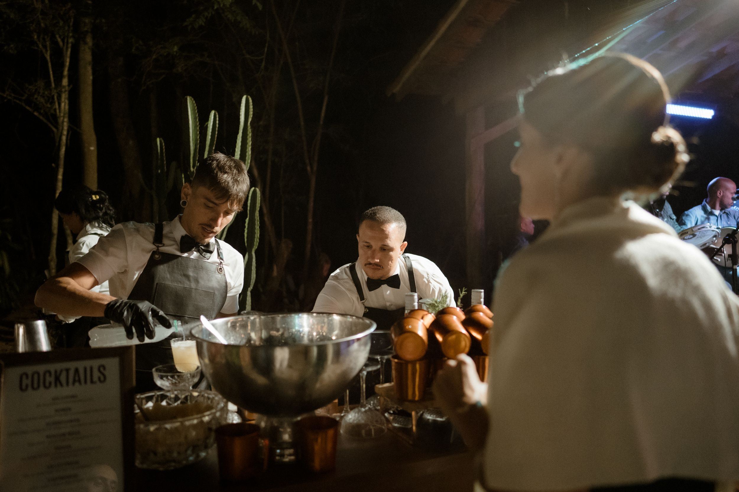 Bartenders preparing drinks at a dimly lit cocktail bar with professional equipment and bottles.