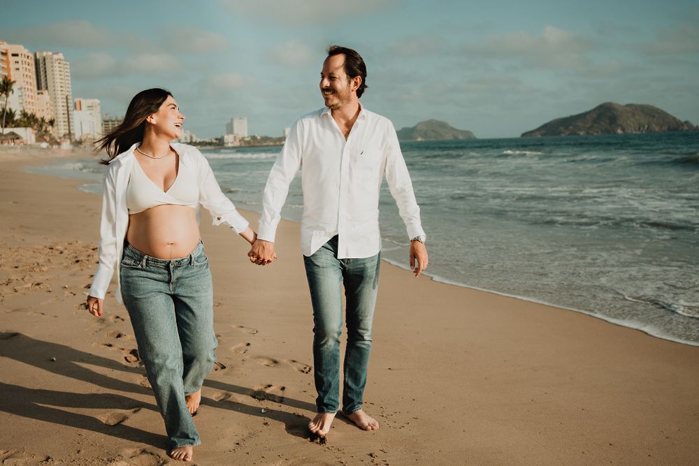 Walking hand in hand along the shore, enjoying their pregnancy journey in Mazatlán