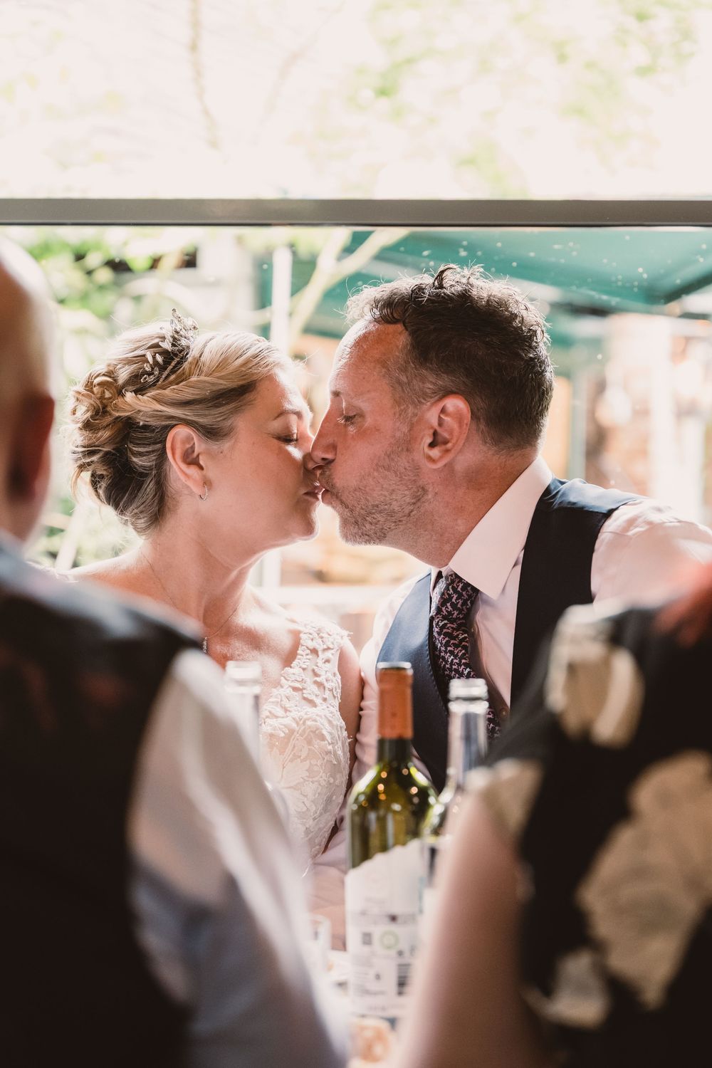 A couple shares an intimate kiss during a wedding reception at an outdoor venue.