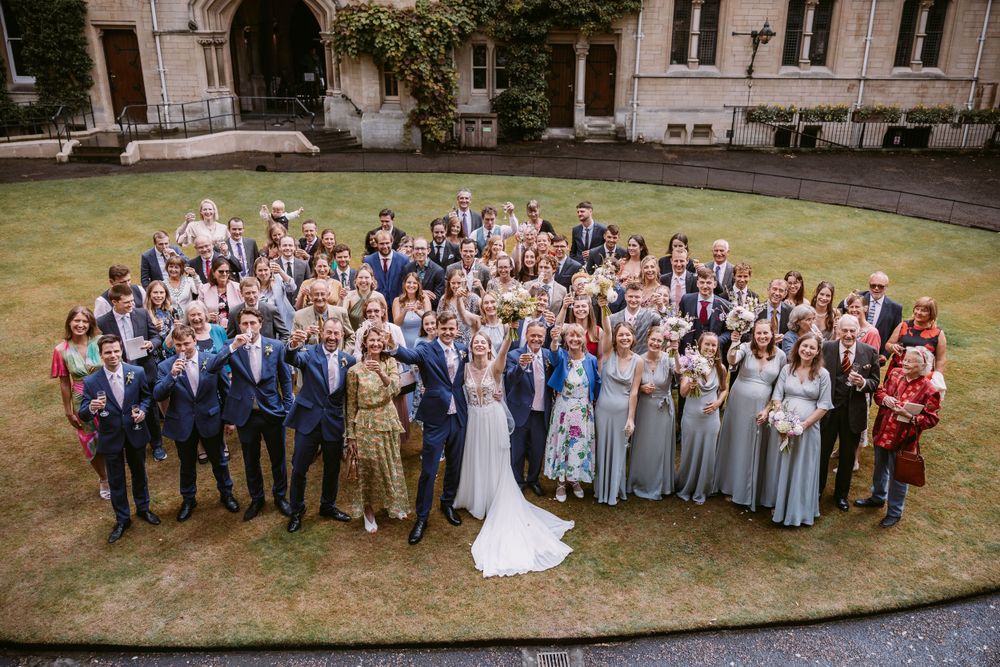Large wedding group photo with guests arranged on lawn of historic building at Balliol College, Oxford